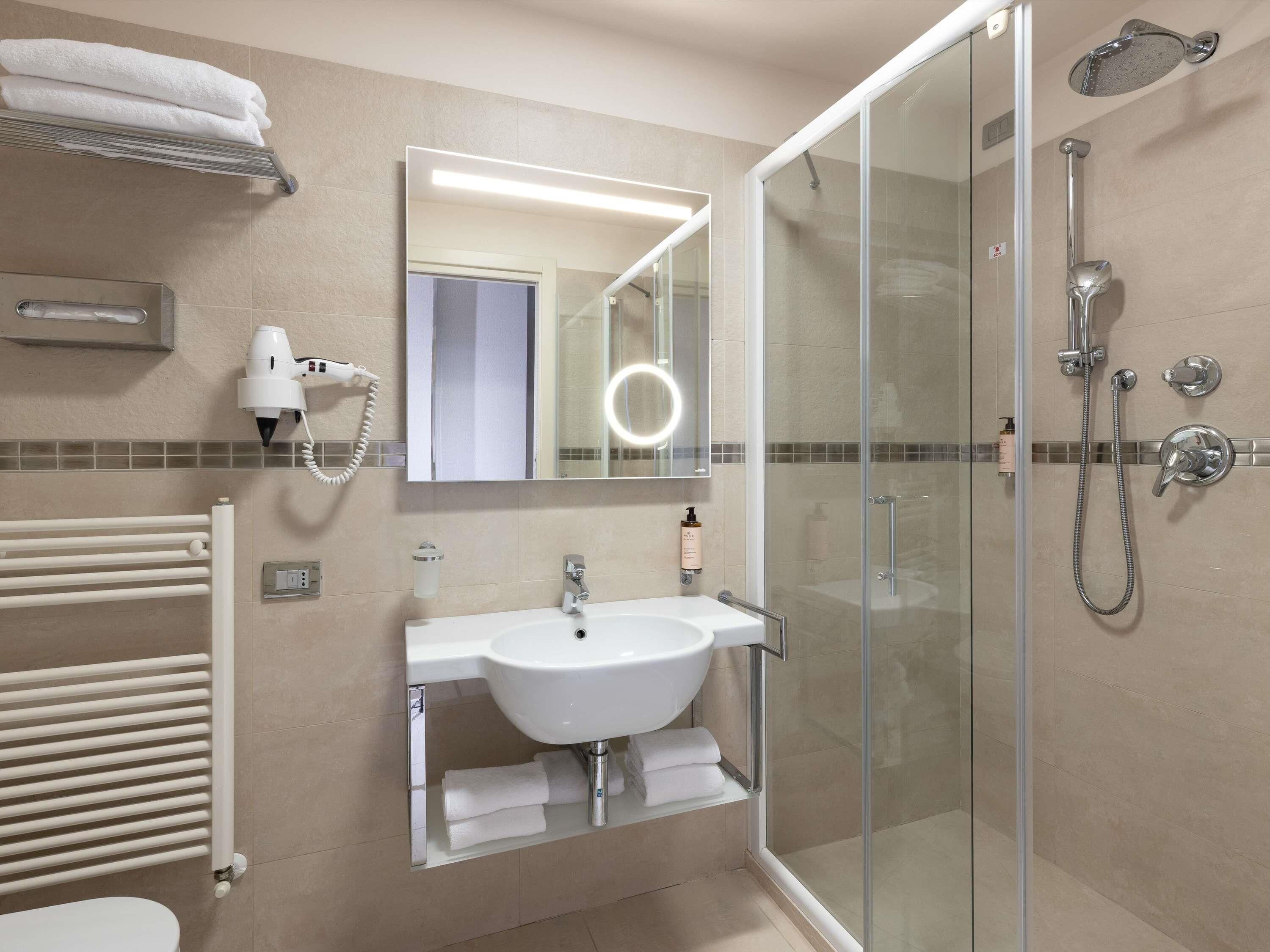 A modern bathroom with a glass-enclosed shower, a white sink, a towel rack, and a hairdryer.