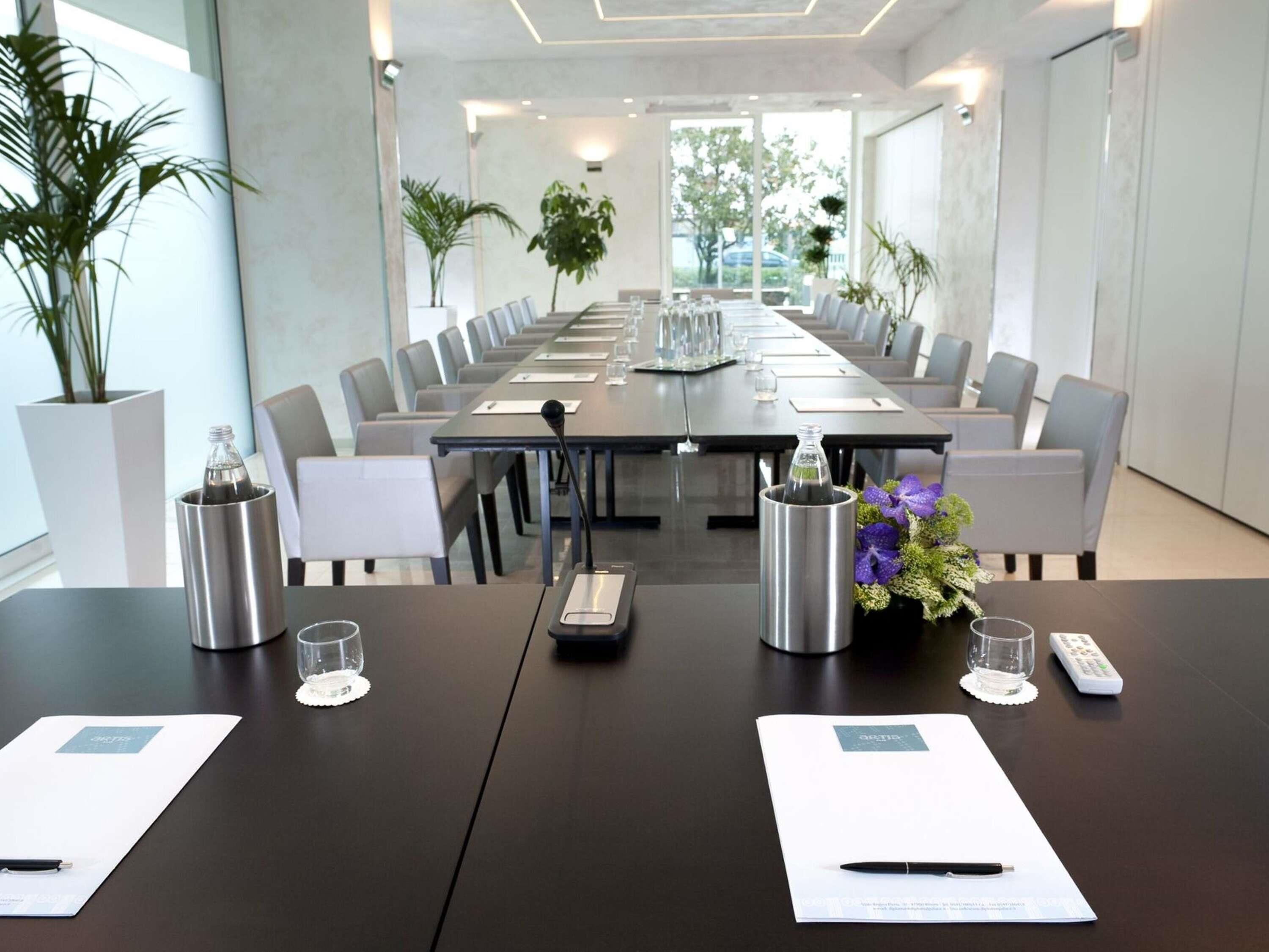 Une salle de conférence avec une longue table, des chaises, des microphones et une plante en pot.