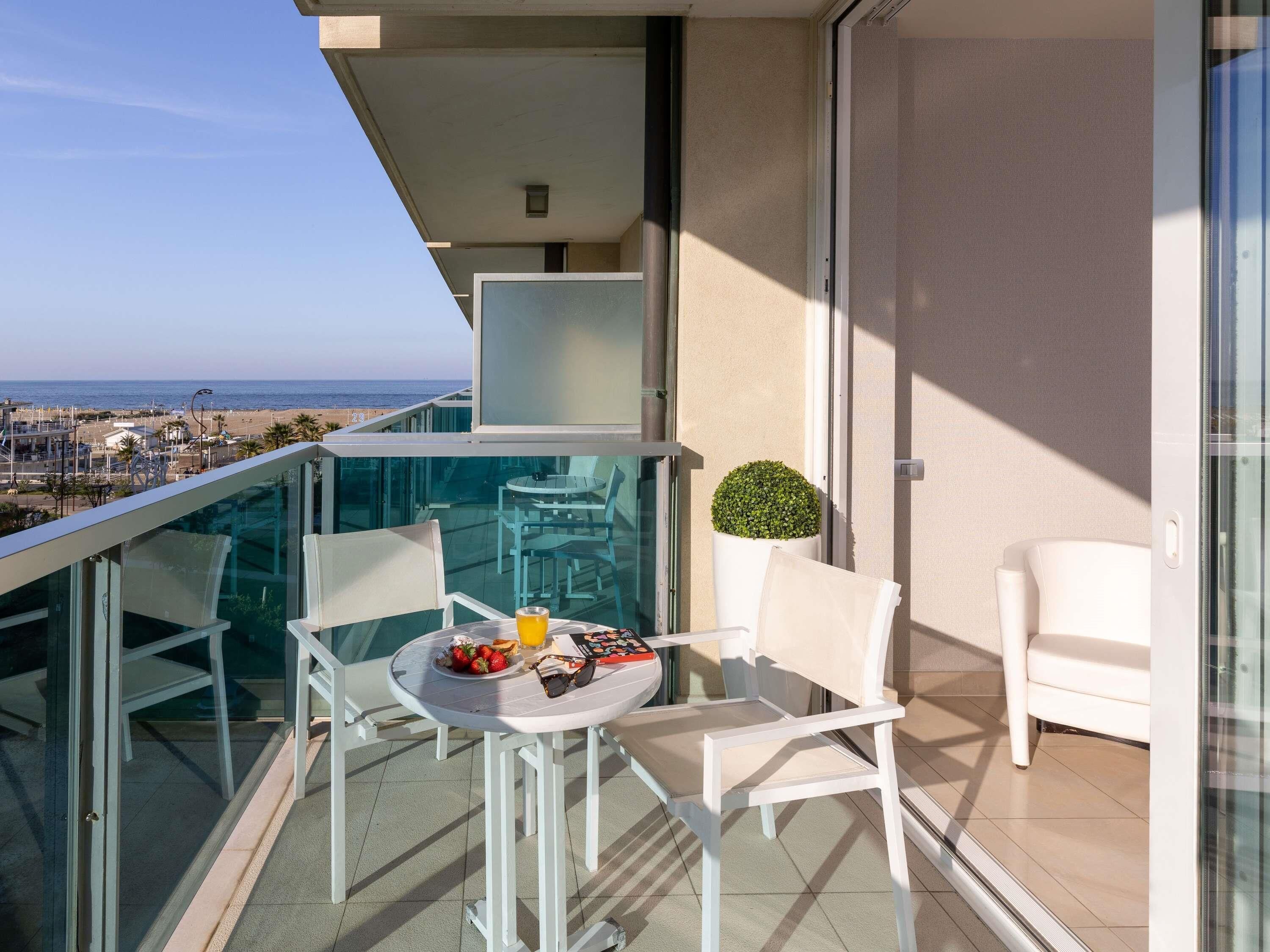 Een balkon met een tafel, stoelen, een kleine plant in pot en uitzicht op zee.