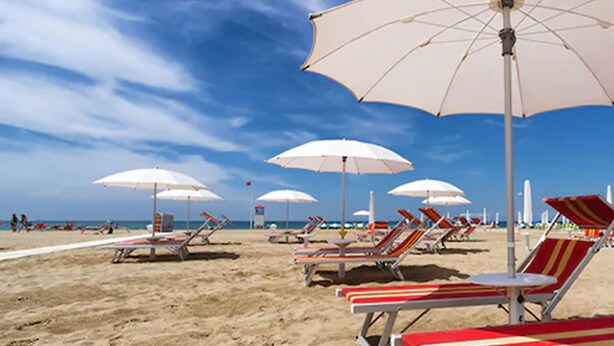 A beach with rows of sun loungers and white umbrellas. - Mercure Rimini Artis (Rimini)