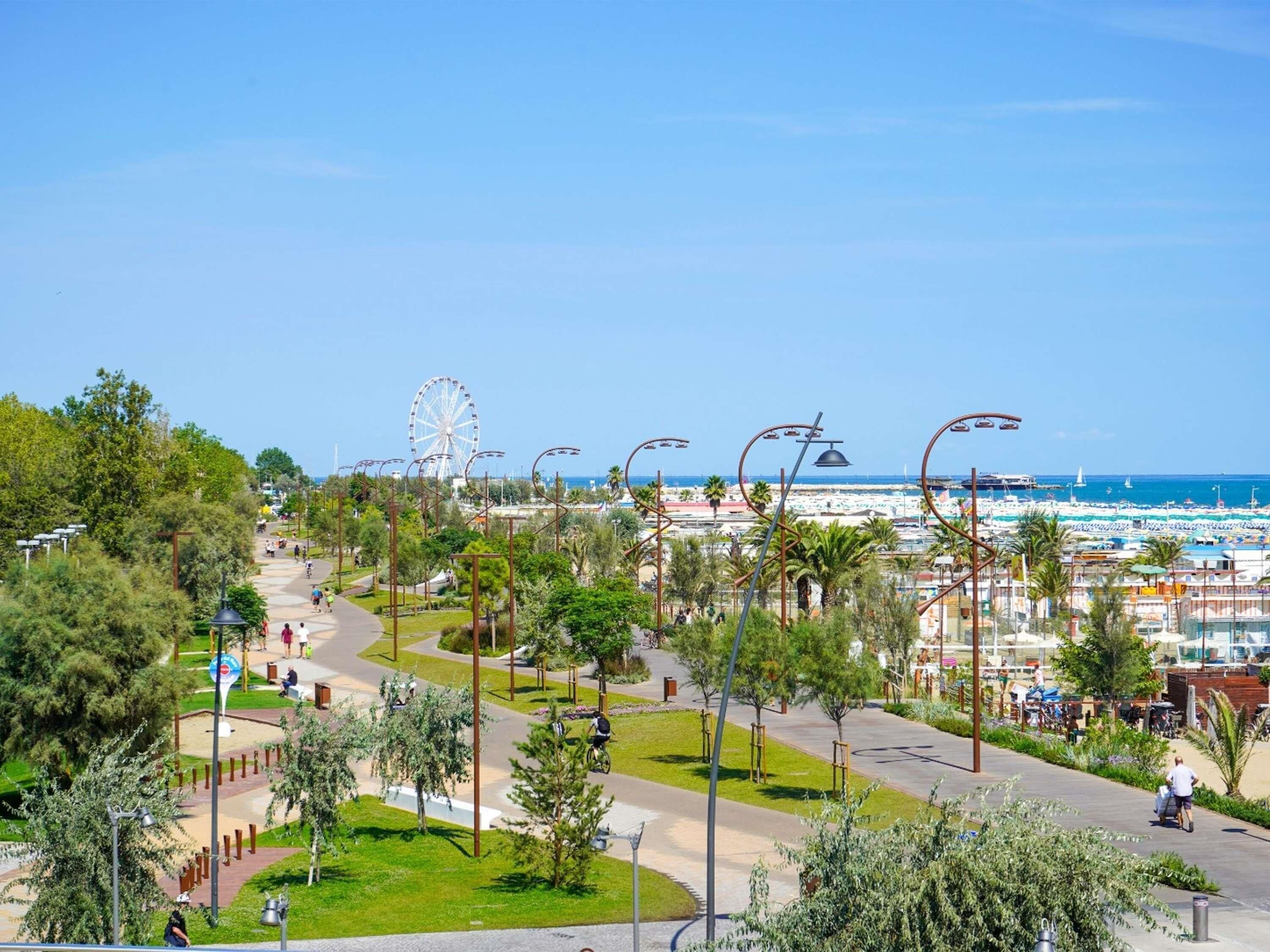 A coastal promenade with a Ferris wheel, palm trees, and a beach in the background.