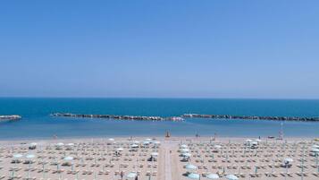 Una spiaggia con file di lettini e ombrelloni, cielo sereno e mare calmo.