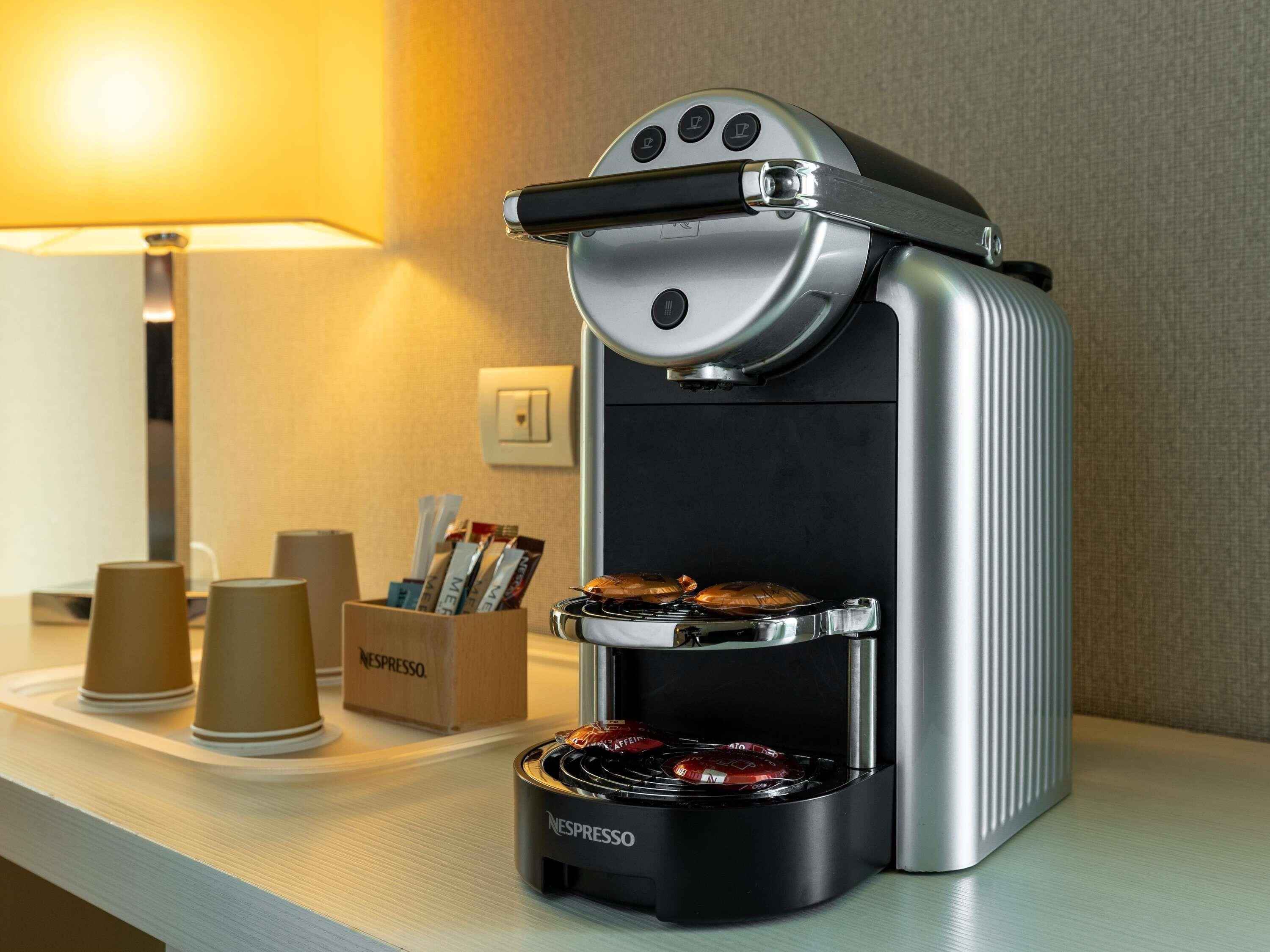 Een Nespresso koffiemachine met een waterreservoir, een lekbak en een houder voor koffiekapsules.