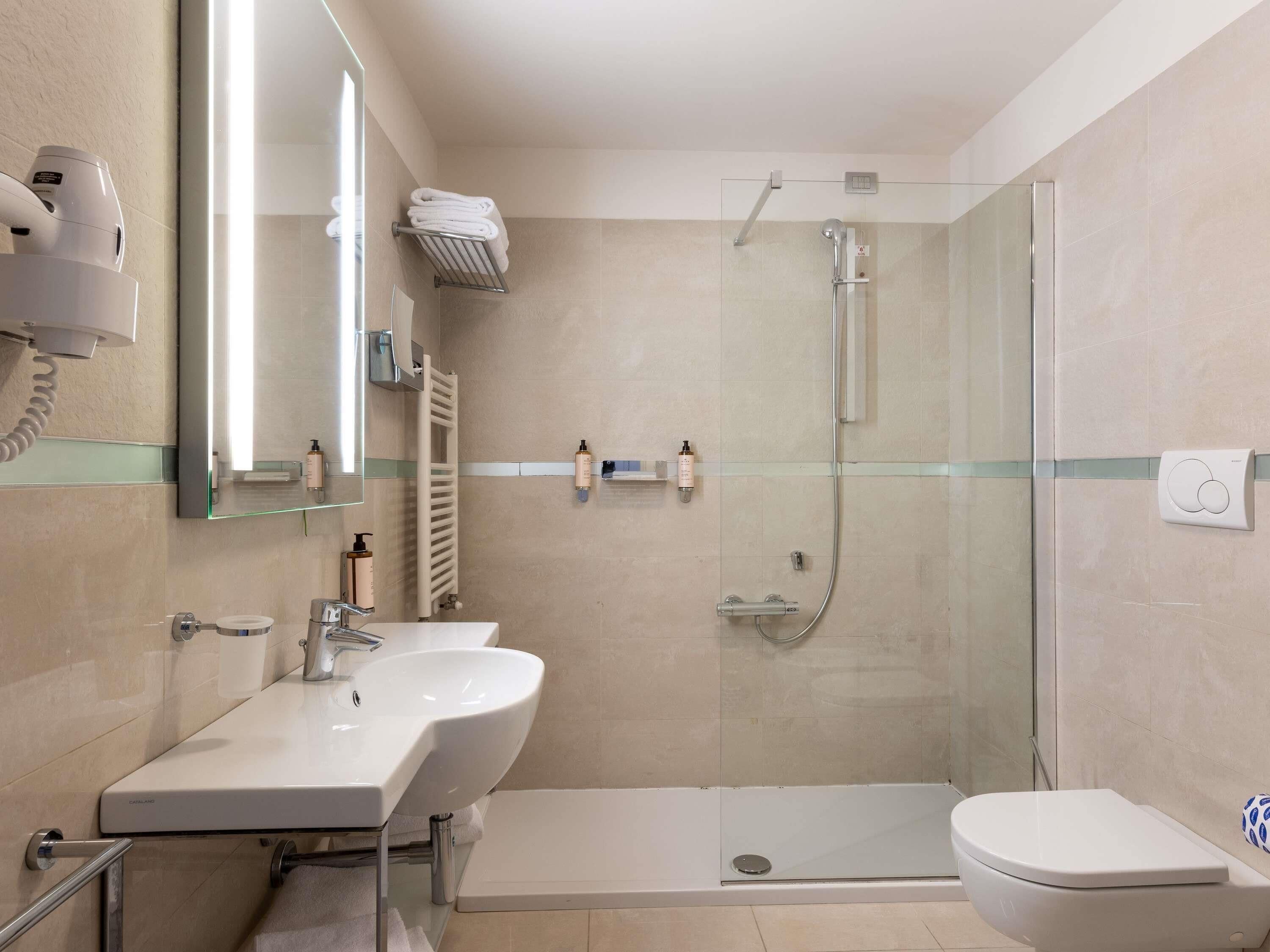 Un baño moderno con ducha de vidrio, tocador con lavamanos y un inodoro.