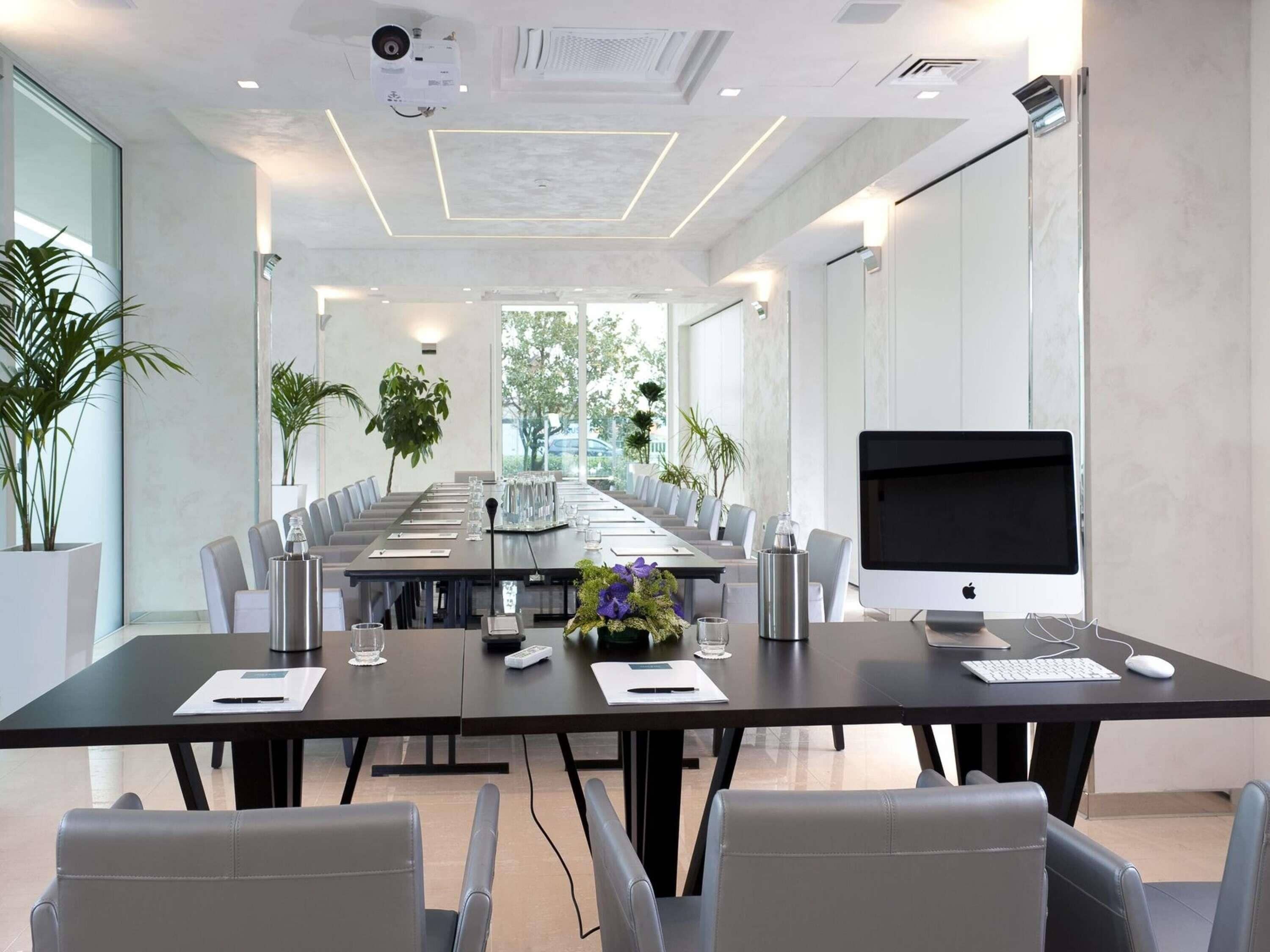A conference room with a long table, chairs, a large screen, and plants.