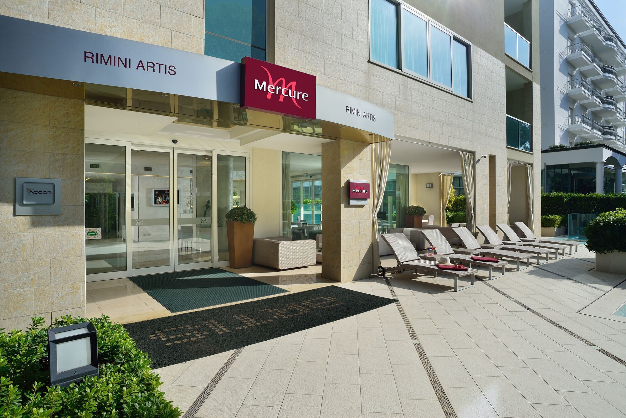 A modern building with a 'Mercure' sign, a glass entrance, and a lounge area with sun loungers.
