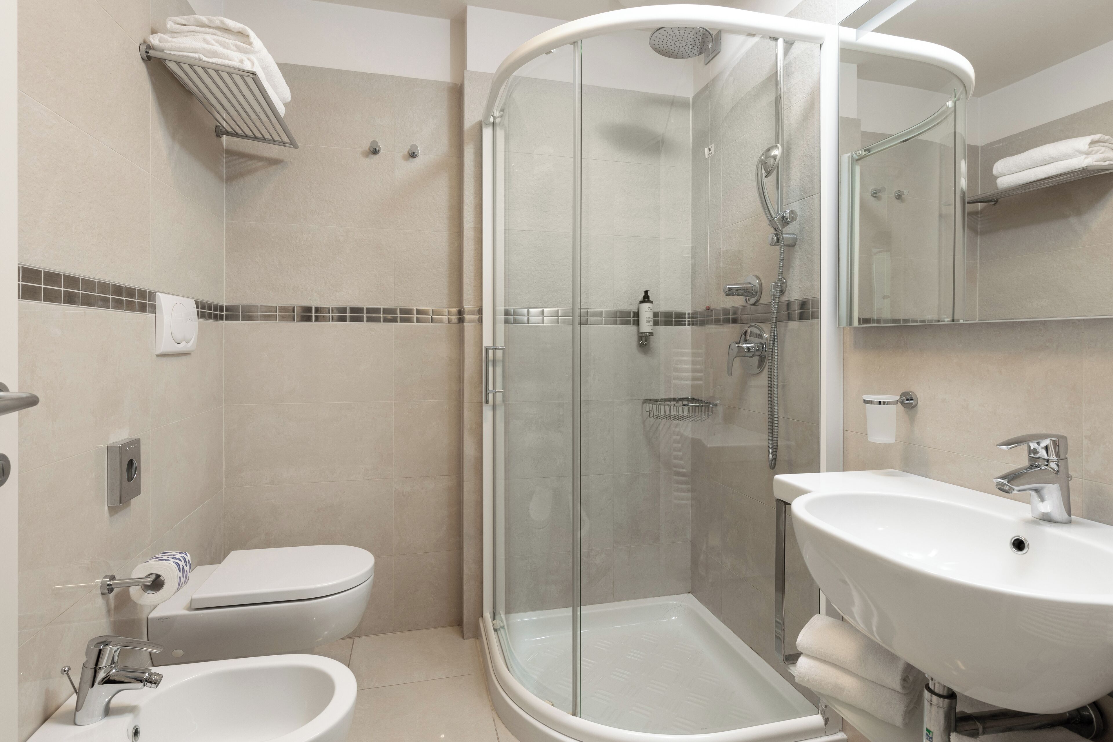 A modern bathroom with a glass-enclosed shower, a white sink, a toilet, and a towel rack.