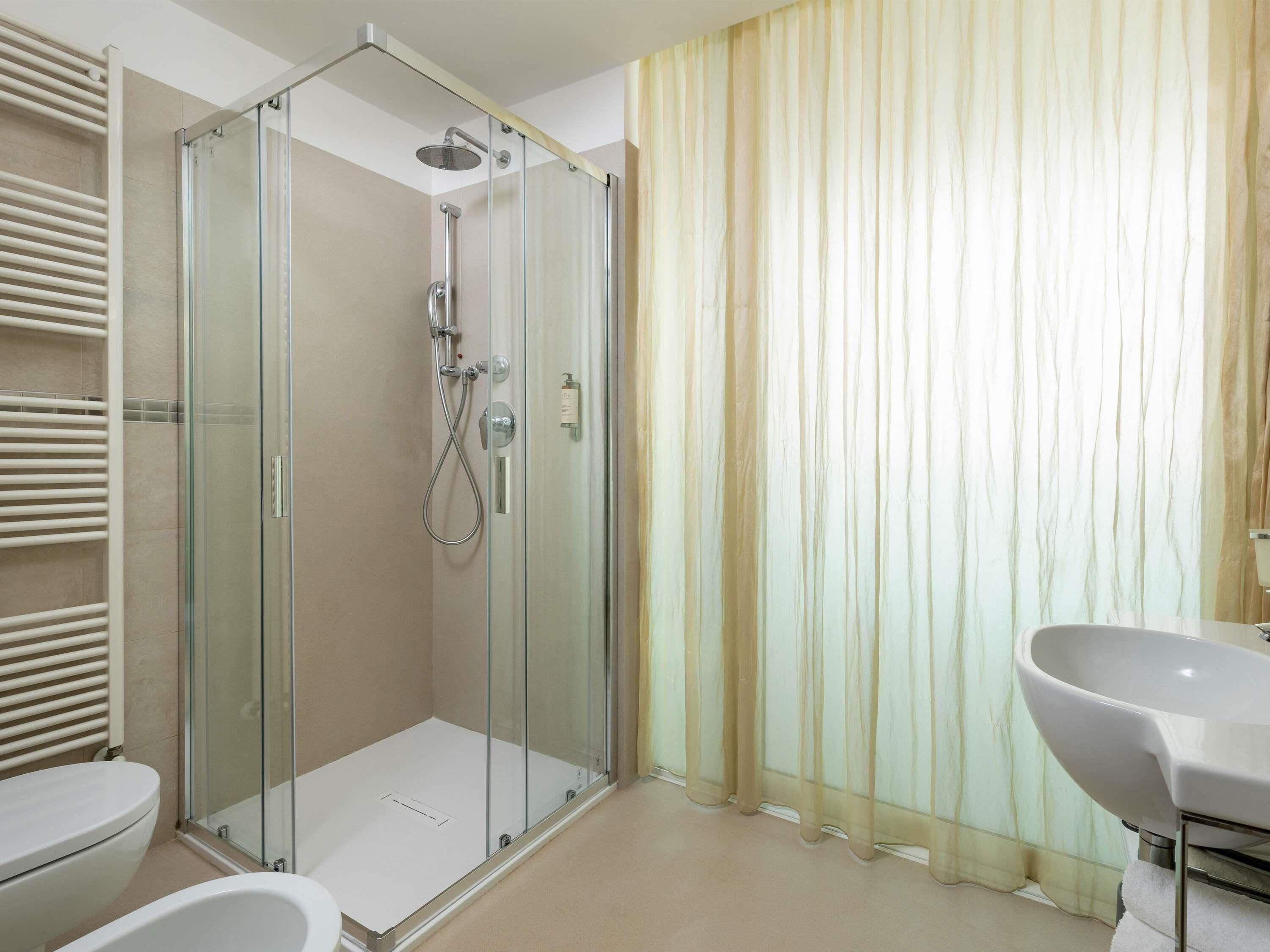 Un baño moderno con cabina de ducha de vidrio, un lavabo blanco y suelo color beige.