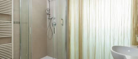 Un baño moderno con cabina de ducha de vidrio, un lavabo blanco y suelo color beige.