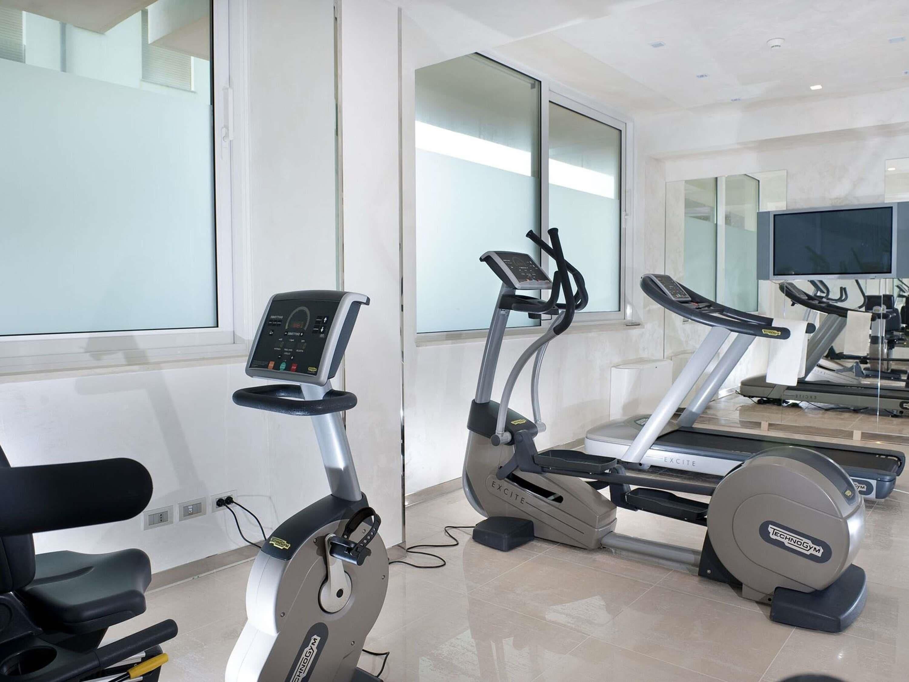 A modern gym with stationary bikes, treadmills, and a mirrored wall.