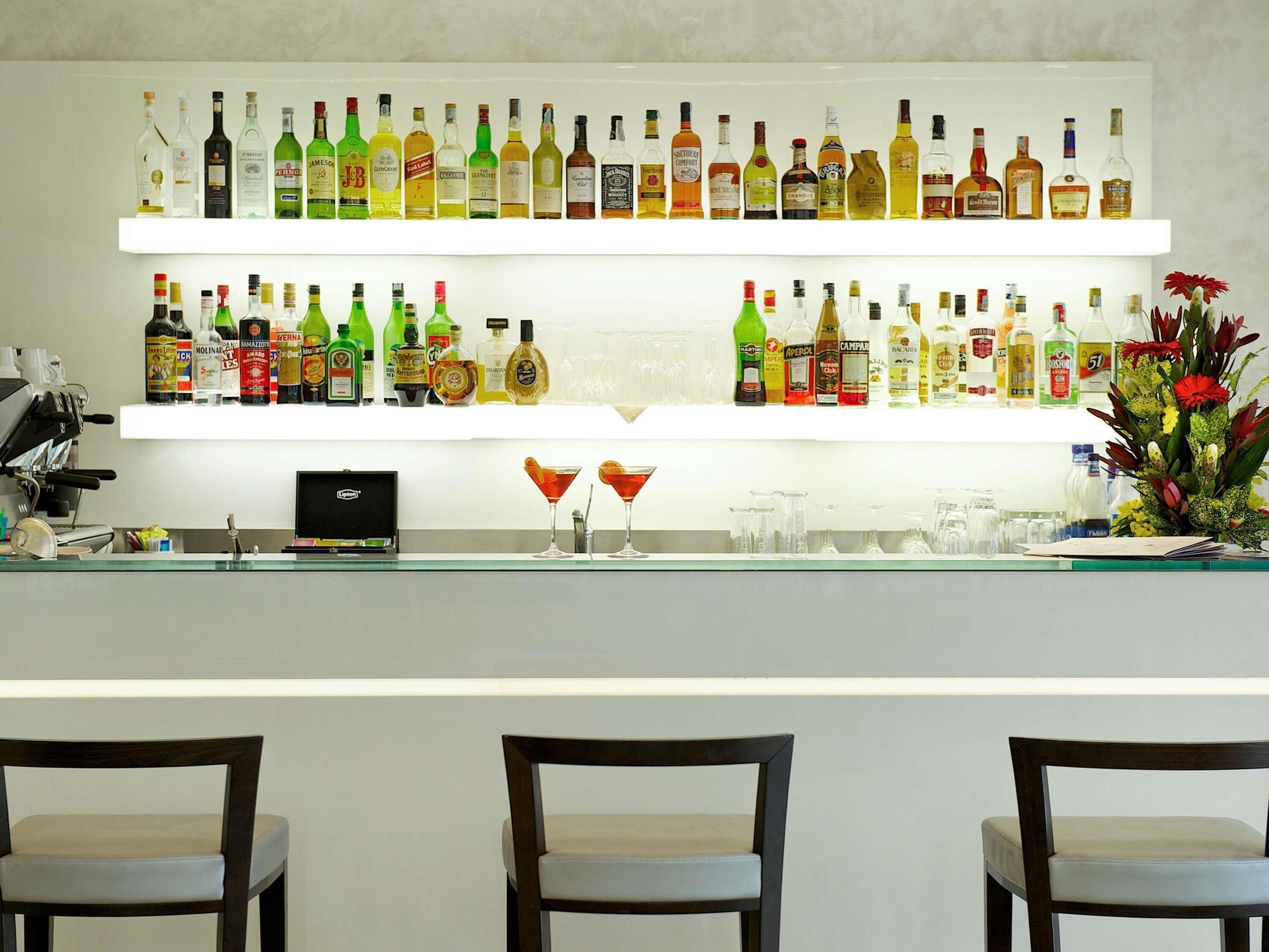 A bar area with multiple shelves of liquor bottles, two chairs, and a bar counter.