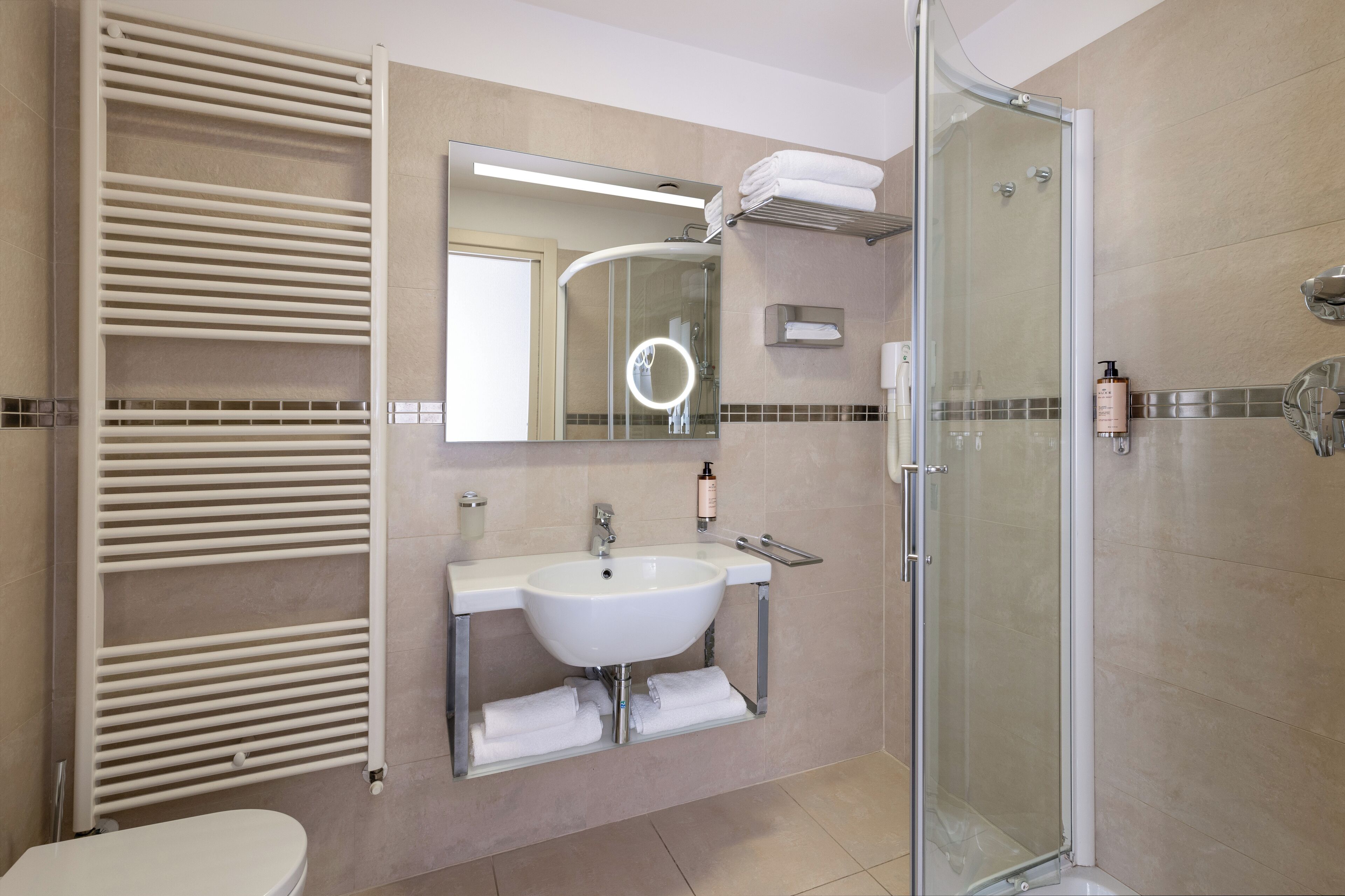 Un baño moderno con ducha de vidrio, lavamanos blanco y perchero para toallas.