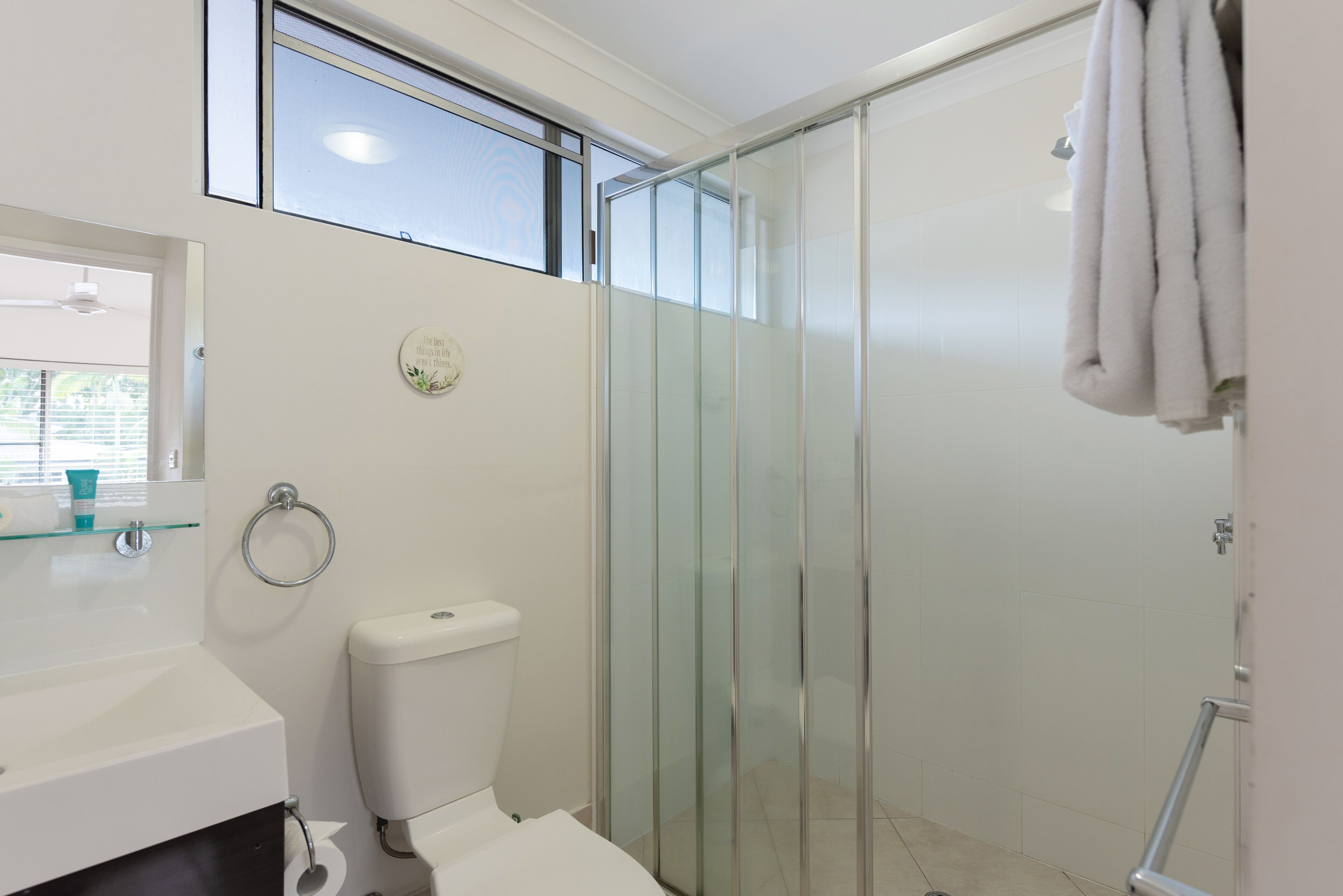 Un bany modern amb plat de dutxa de vidre, vàter i un lavabo amb prestatge de vidre.