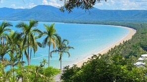A beach with clear turquoise water, palm trees, and mountains in the background. - Lychee Tree Holiday Apartments (Port Douglas)