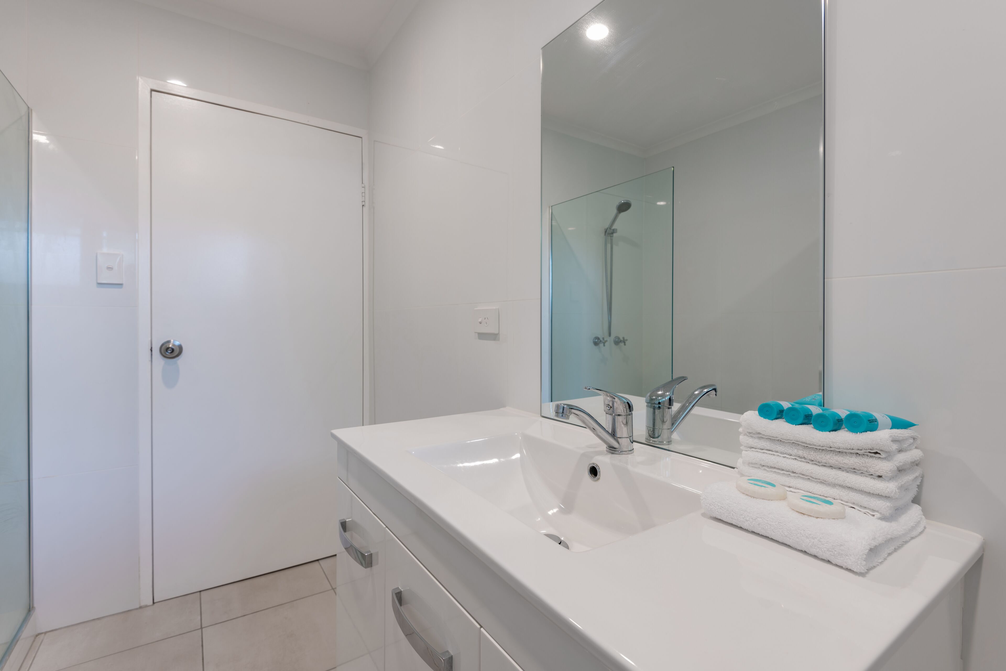 Une salle de bain moderne avec un lavabo blanc, une douche en verre et un miroir au-dessus du lavabo.