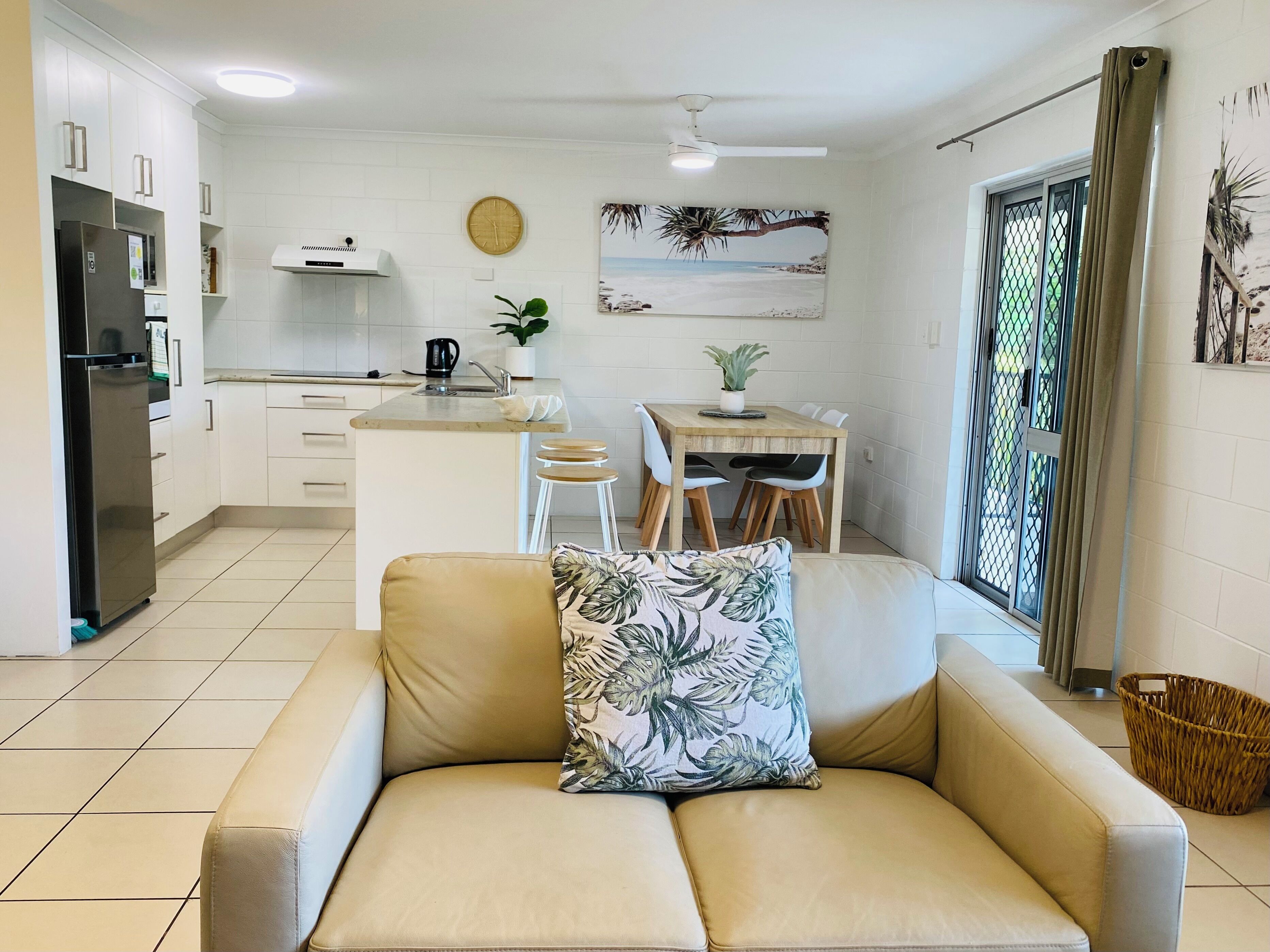 A modern kitchen with white cabinets, a refrigerator, and a dining area with a wooden table and chairs.