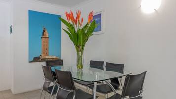 A modern dining area with a glass table and black chairs, a decorative vase with flowers, and a framed picture of a tower on the wall.