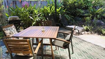 Une terrasse extérieure avec une table et des chaises en bois, entourée d’une végétation luxuriante et d’une clôture en bois.