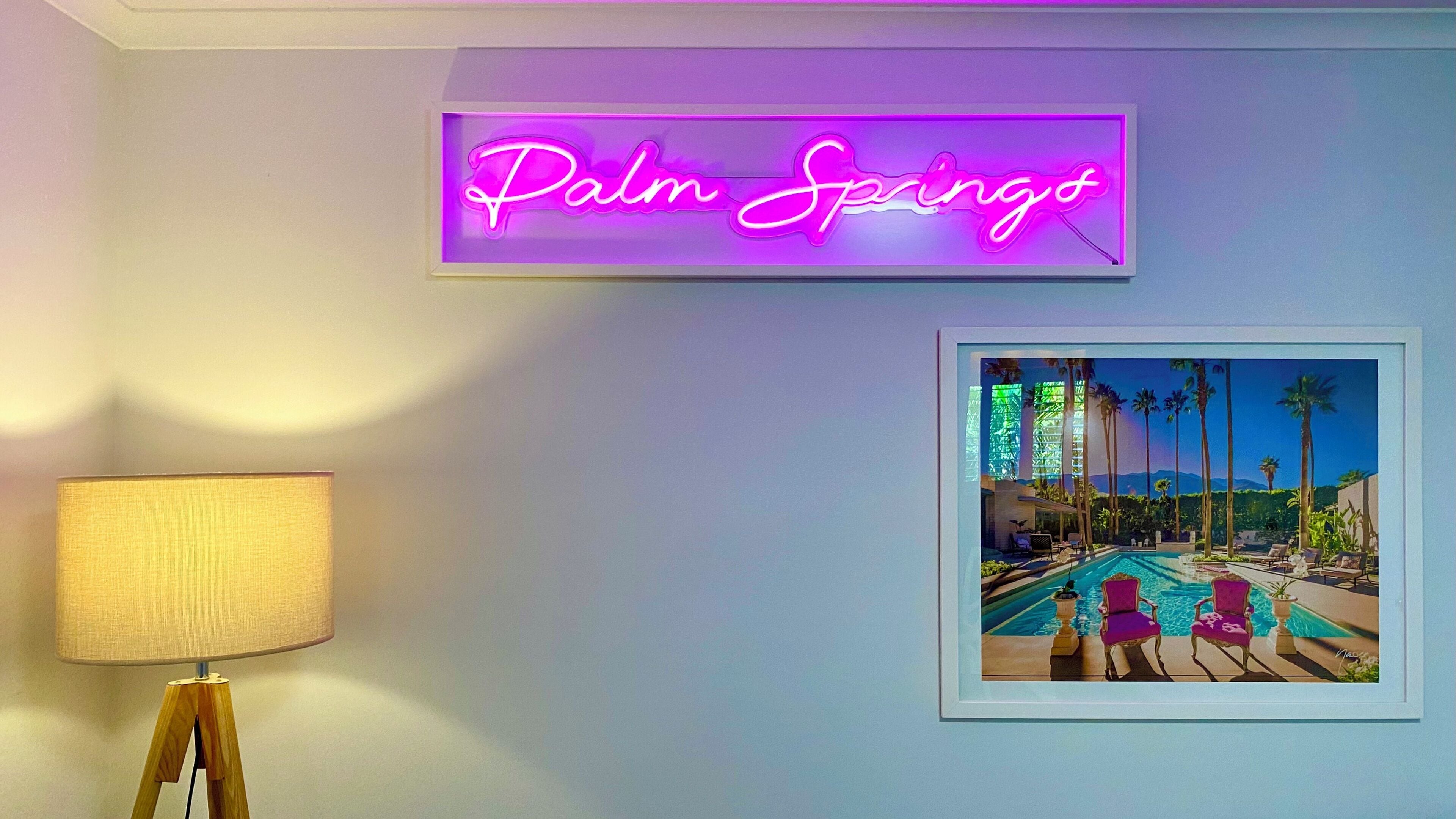 Un letrero de neón con la leyenda 'Palm Springs' y un cuadro enmarcado que muestra una escena junto a la piscina.