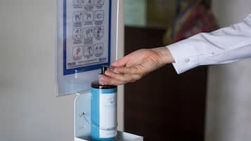A hand dispensing gel from a dispenser mounted on a wall.