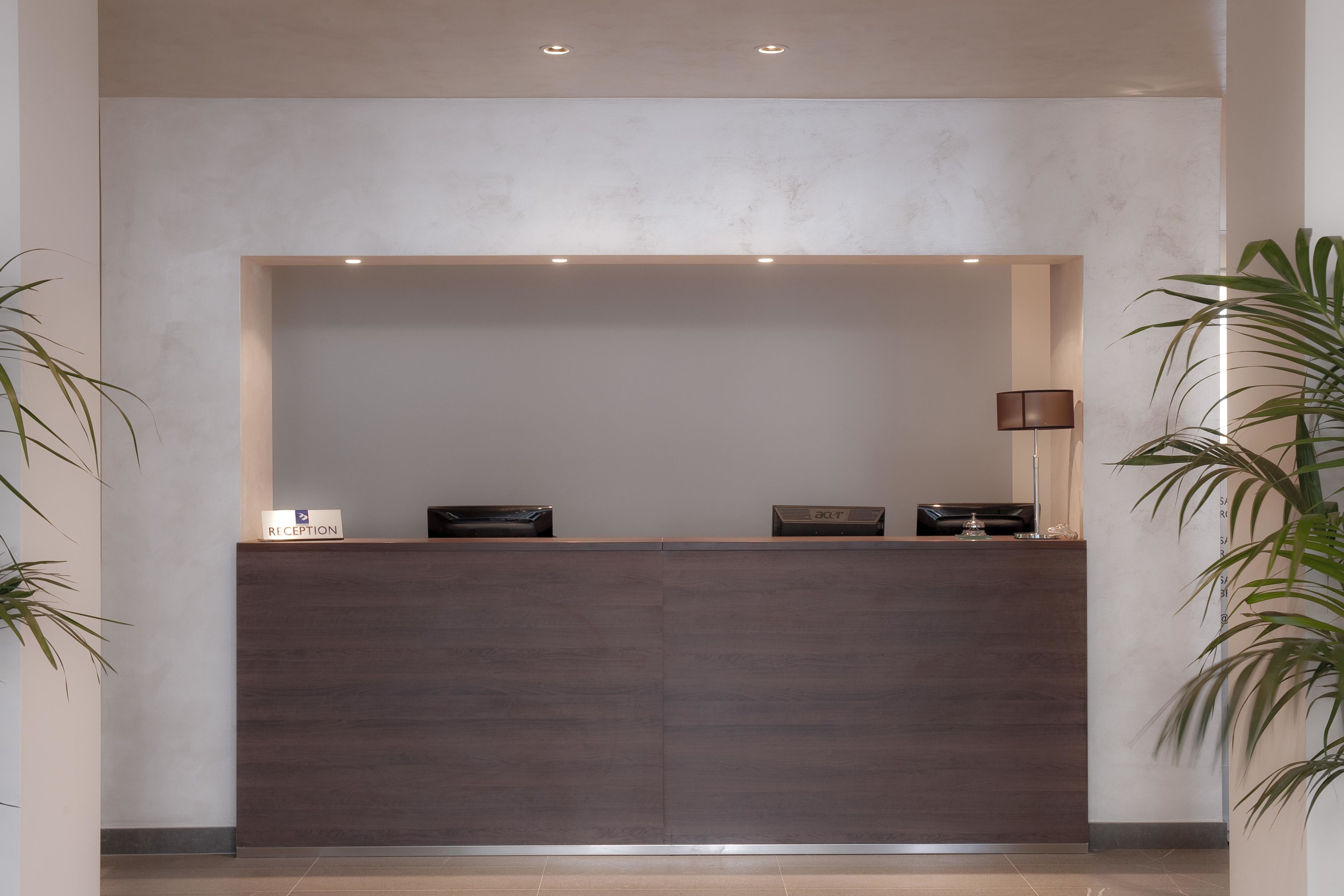 A reception desk with a dark wood finish, a 'Reception' sign, and a lamp to the right.