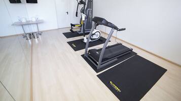 Un gimnasio con equipamiento de ejercicio, un escritorio con sillas y una puerta.