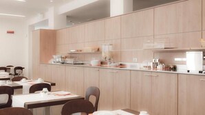 Un comedor de hotel moderno con armarios de madera clara, una barra larga y varias mesas con sillas.