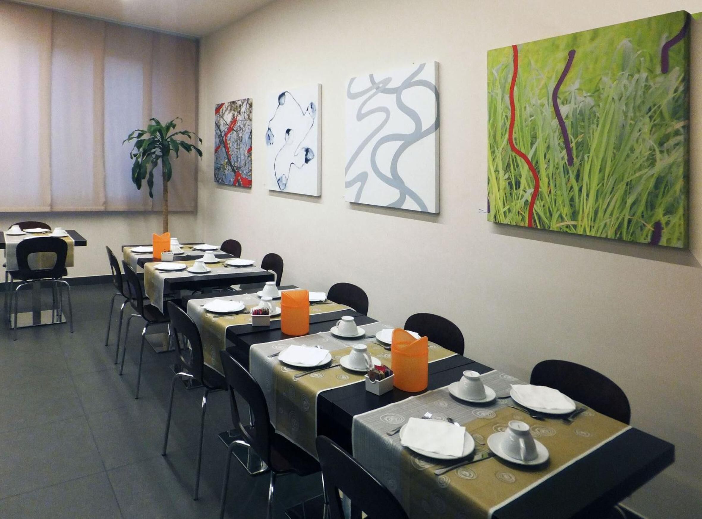 A dining area with tables set for service, a potted plant, and abstract art on the walls.