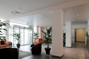 A spacious lobby with a modern design, featuring a reception desk, seating area with chairs and a sofa, and potted plants. - Blu Arena Hotel (Vallefoglia)