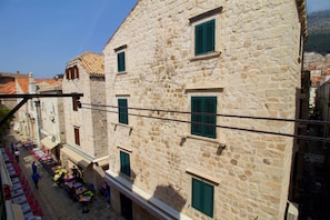 Ein Gebäude aus Stein mit grünen Fensterläden, ein Innenhof mit Tischen und Stühlen und einem strahlend blauen Himmel.