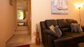 A living room with a black leather sofa, a painting of sailboats, and a vase with branches. - Divine Apartments (Dubrovnik)