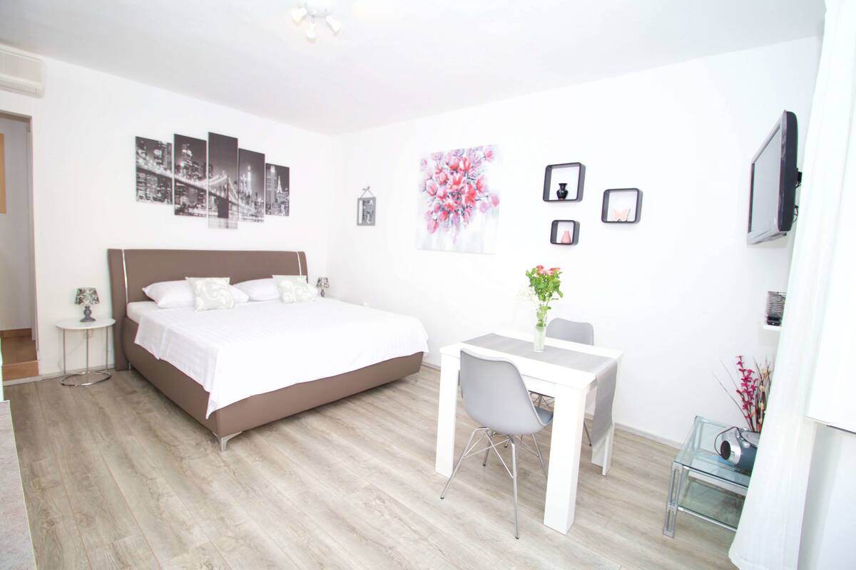 A bedroom with a bed, a desk, and a chair. There are wall decorations and a TV.