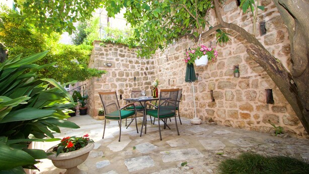 A stone courtyard with a table and chairs, surrounded by potted plants and a hanging flower basket. - Divine Apartments (Dubrovnik)