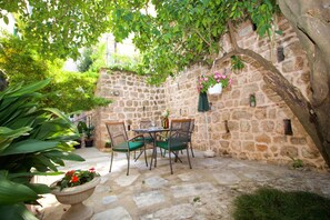 A stone courtyard with a table and chairs, surrounded by potted plants and a hanging flower basket. - Divine Apartments (Dubrovnik)