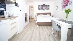 A modern hotel room with a bed, a desk, a chair, a kitchenette, and a bathroom. - Divine Apartments (Dubrovnik)