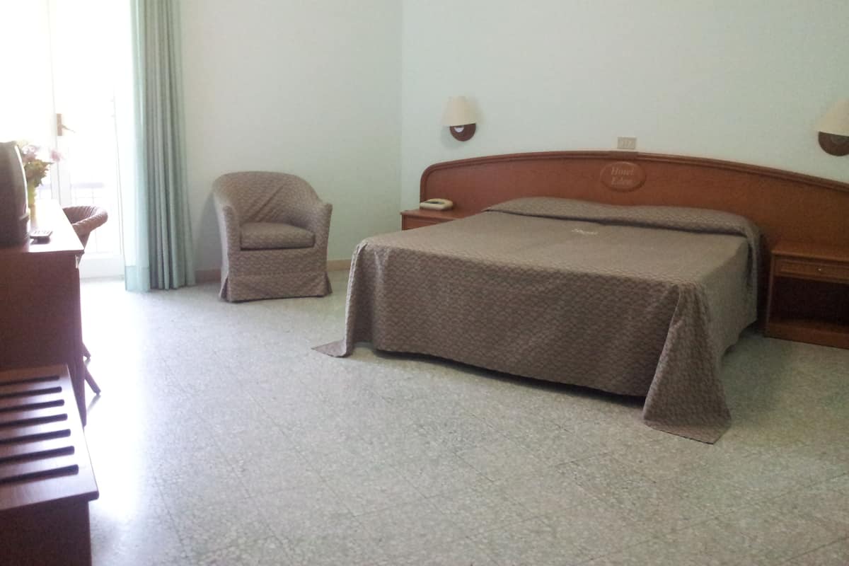 A hotel room with a bed, a chair, a nightstand, and a desk.