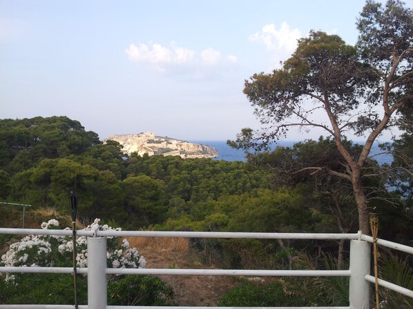 A coastal landscape with a historic fort on a hill, surrounded by dense greenery and a clear sky.