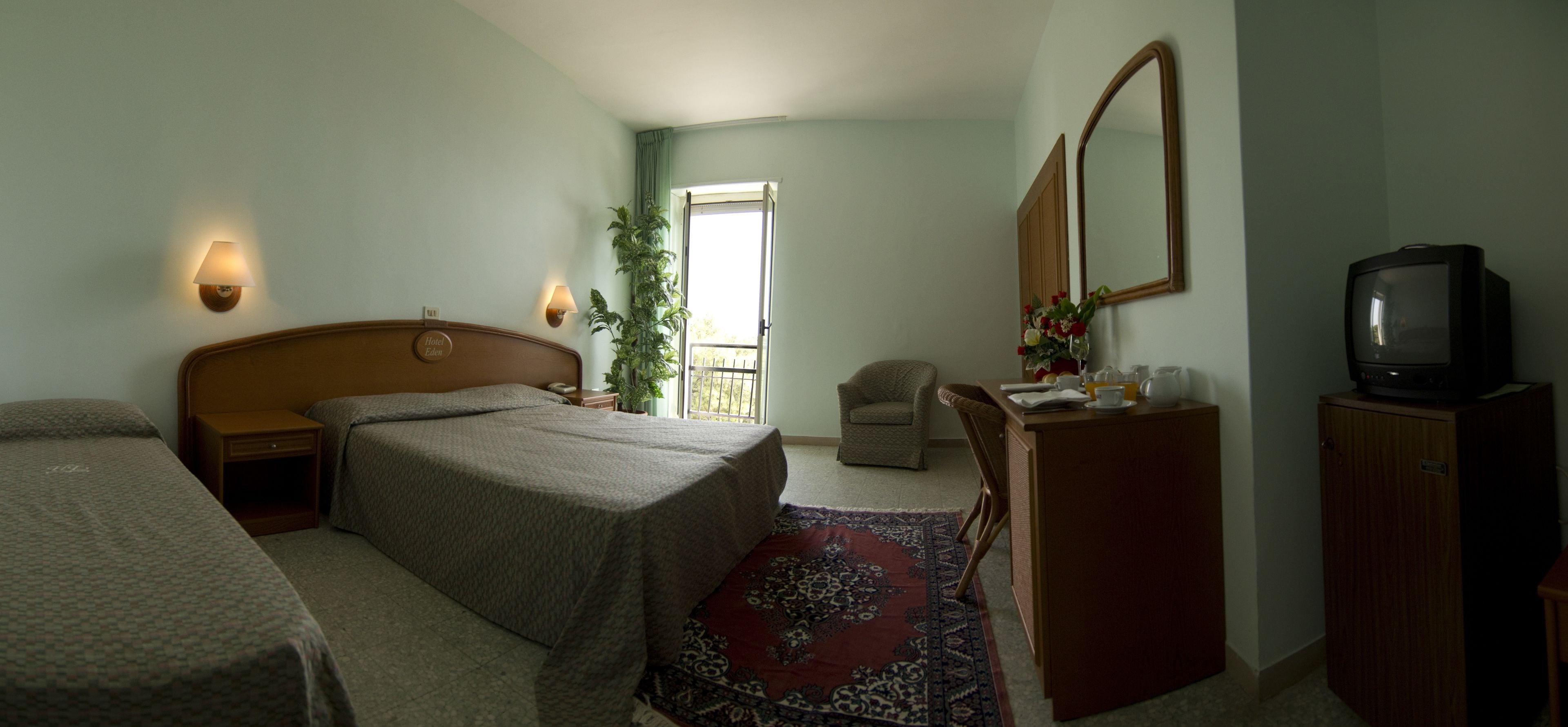 Una camera d'albergo con un letto, comodini, una scrivania con uno specchio, una televisione e una sedia.