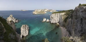 A coastal landscape with rocky cliffs, clear turquoise waters, and a beach.