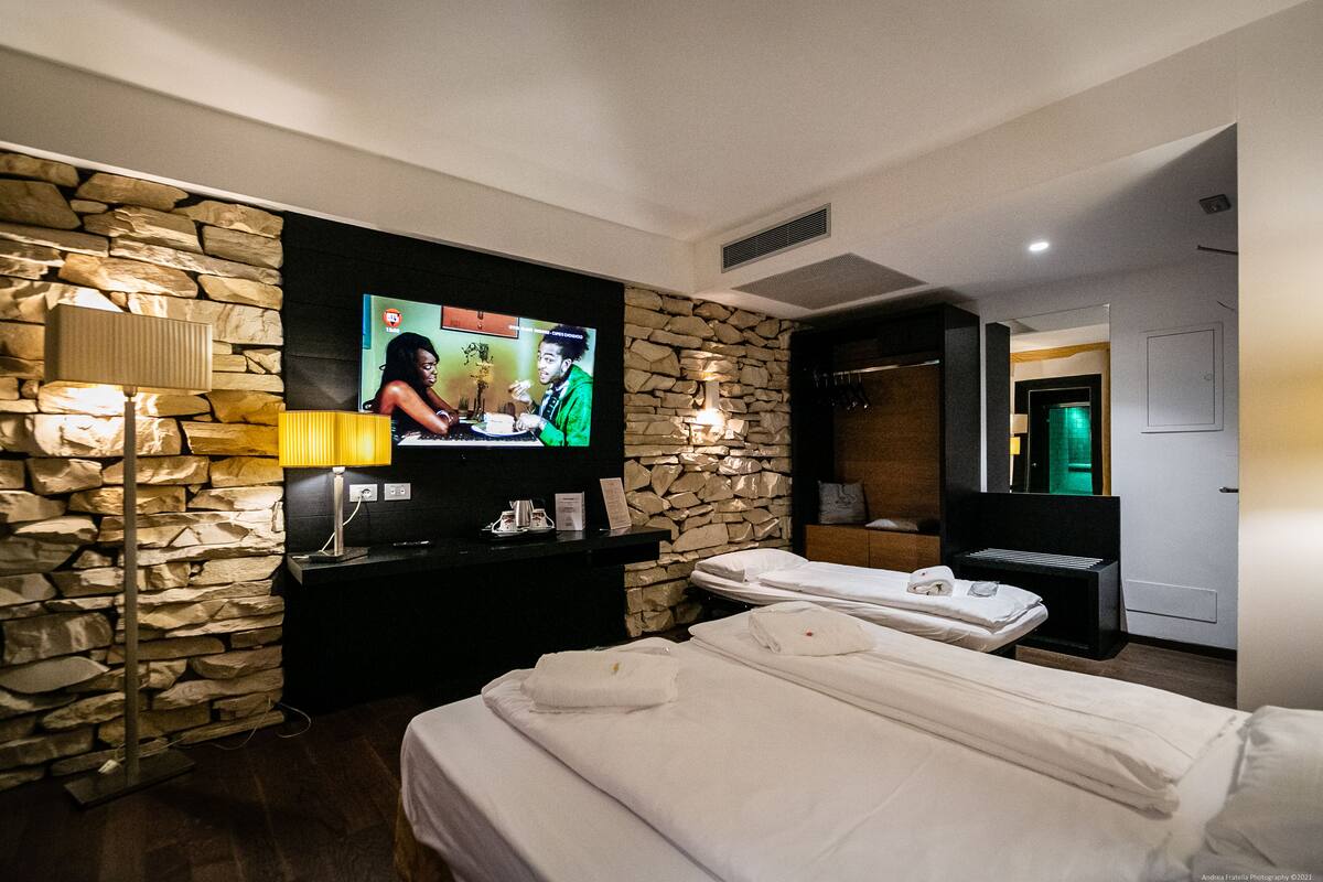 A hotel room with a stone wall, a flat-screen TV, a massage table, and a bed.