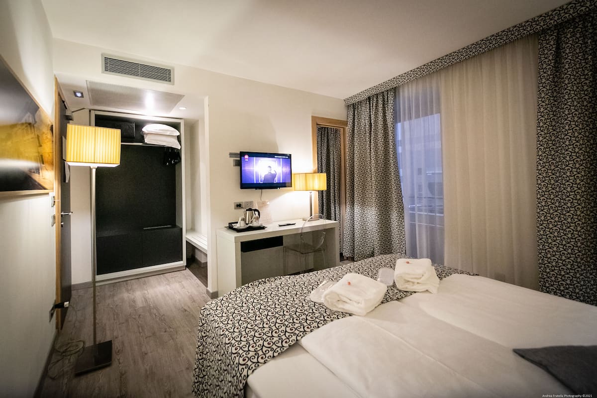 A hotel room with a bed, a desk with a television, a shower, and a window with curtains.