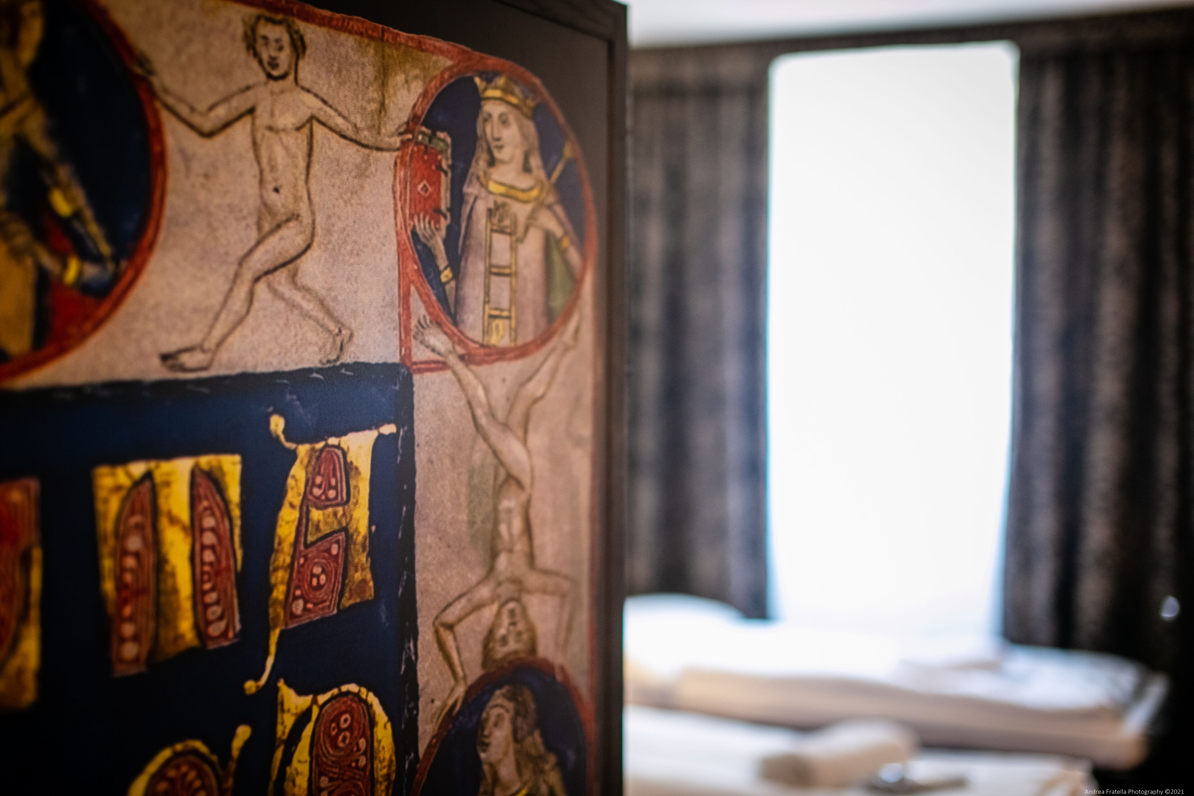 A room with a large medieval-style tapestry on the wall, a bed, and a window with curtains.