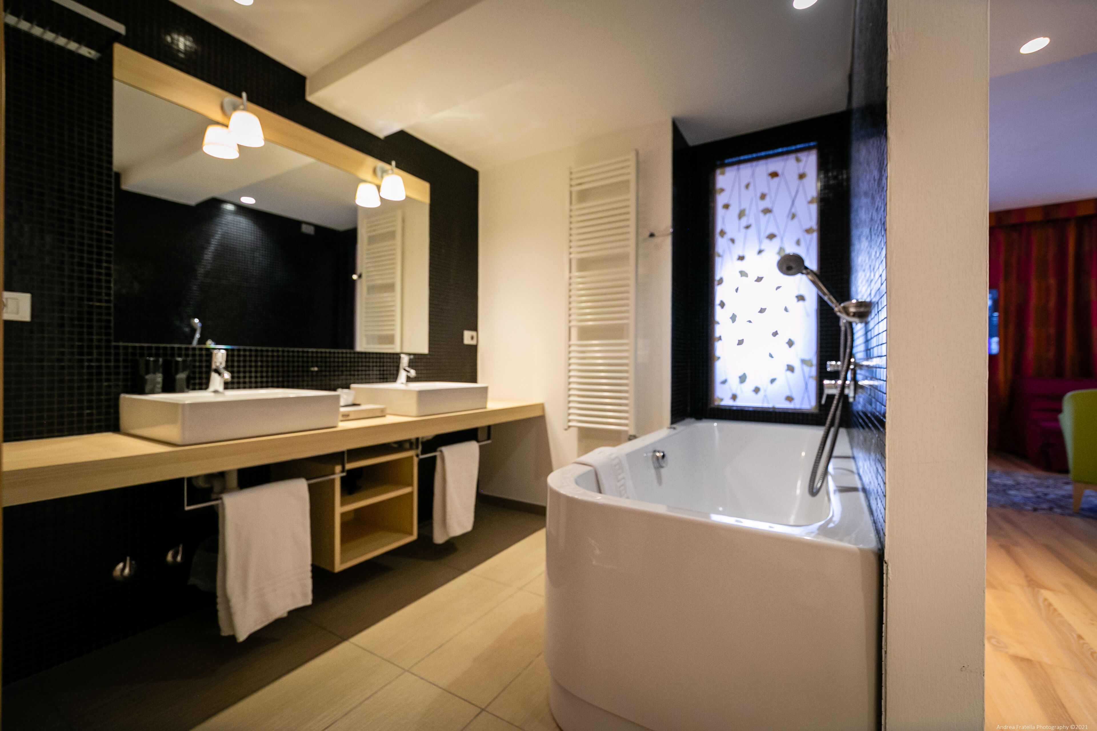 Un baño moderno con dos lavamanos, una bañera grande y un espejo con luces.