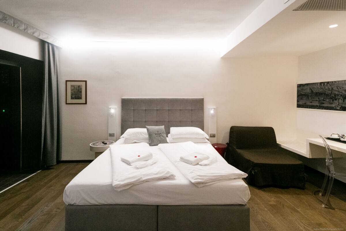 A hotel room with a large bed, bedside tables, a chair, and a desk with a chair.