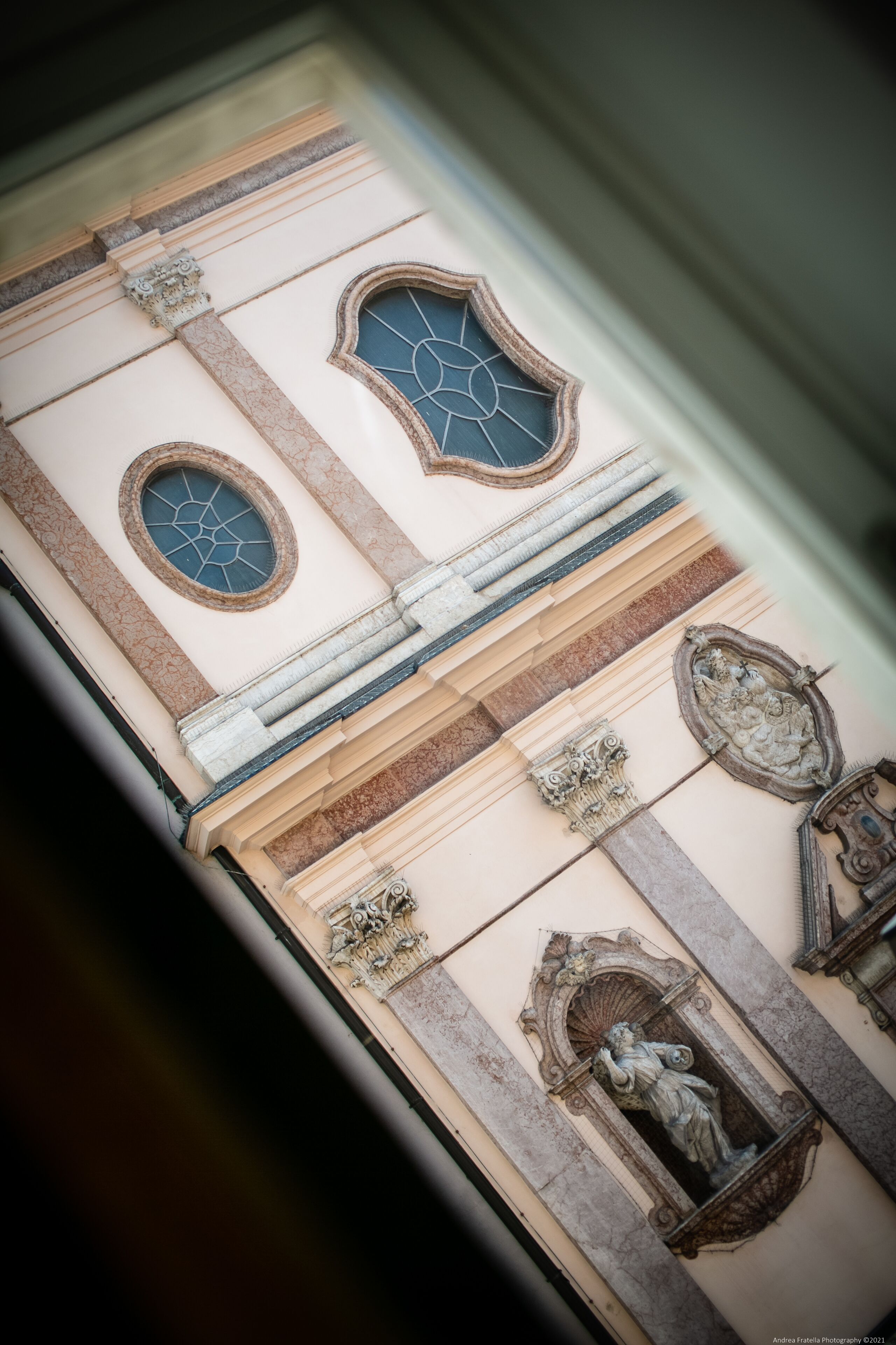 A detailed view of a building's facade with ornate architectural elements, including a statue, decorative moldings, and a window with a geometric pattern.