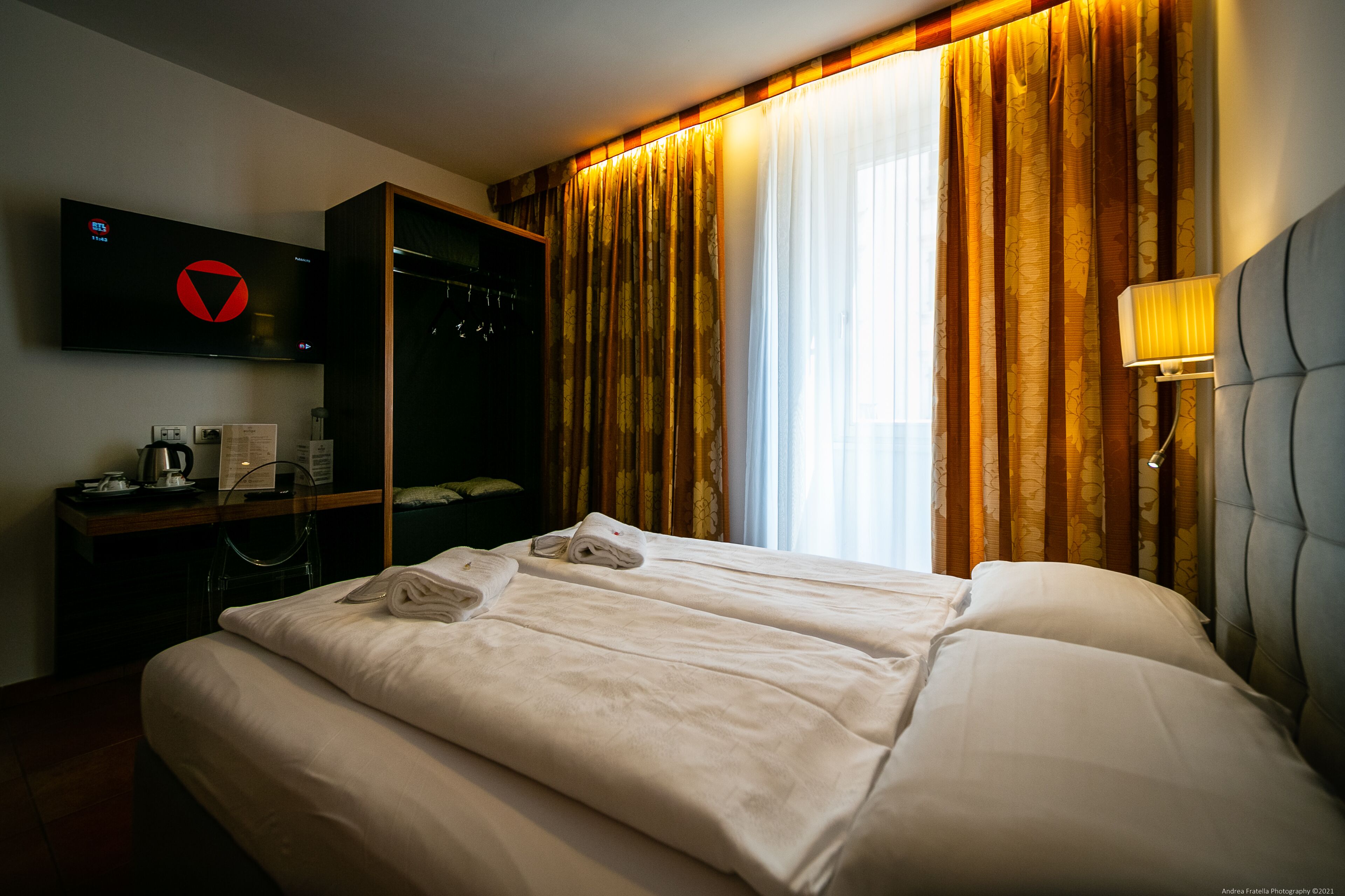 A hotel room with two beds, a TV, a desk with a coffee maker, and a wardrobe.