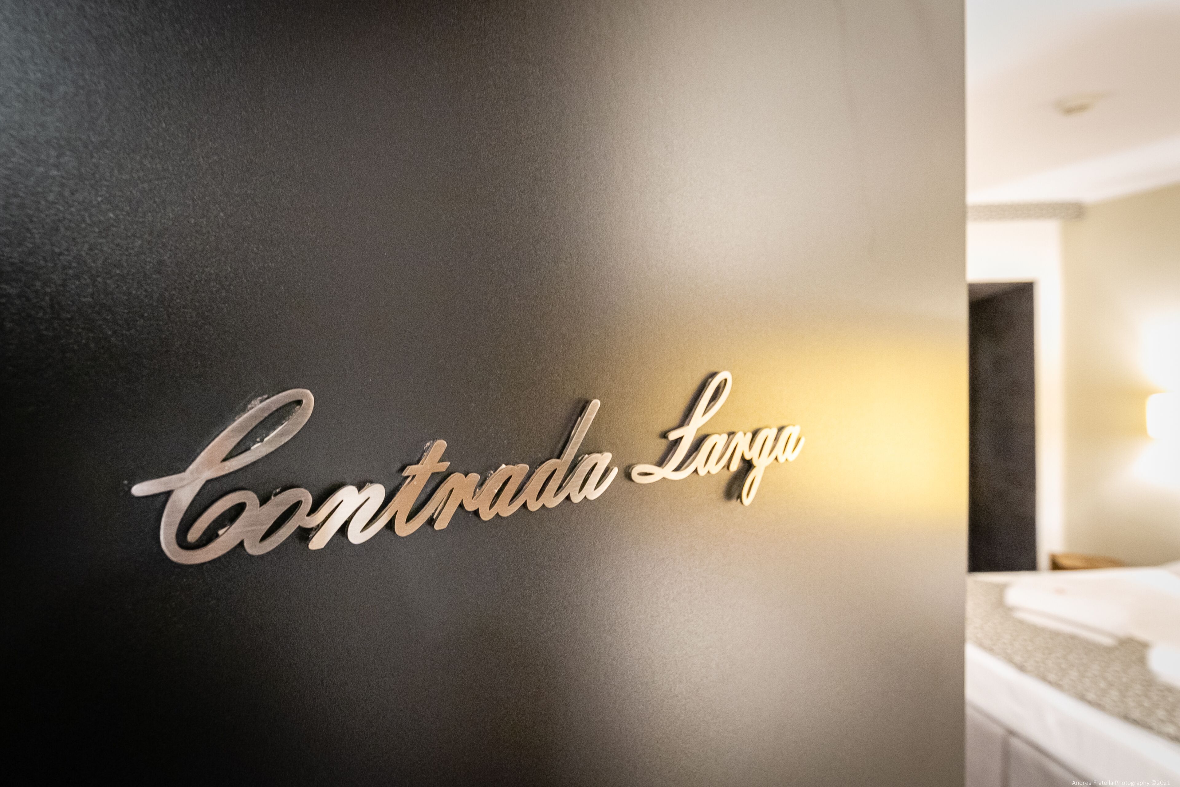 Una pared con un letrero metálico que dice 'Contrada Larga'.