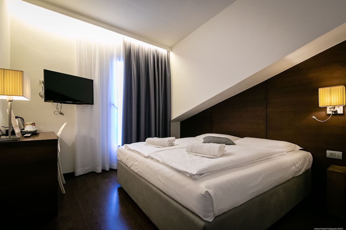 A hotel room with a bed, a desk, a TV, and a window with curtains.
