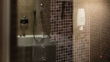 A bathroom with a tiled wall, a glass shower enclosure, and a white soap dispenser.