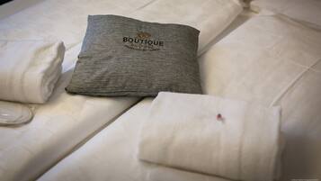 En snyggt bäddad säng med en grå kudde där ordet ”BOUTIQUE” är broderat och en vikt vit handduk.